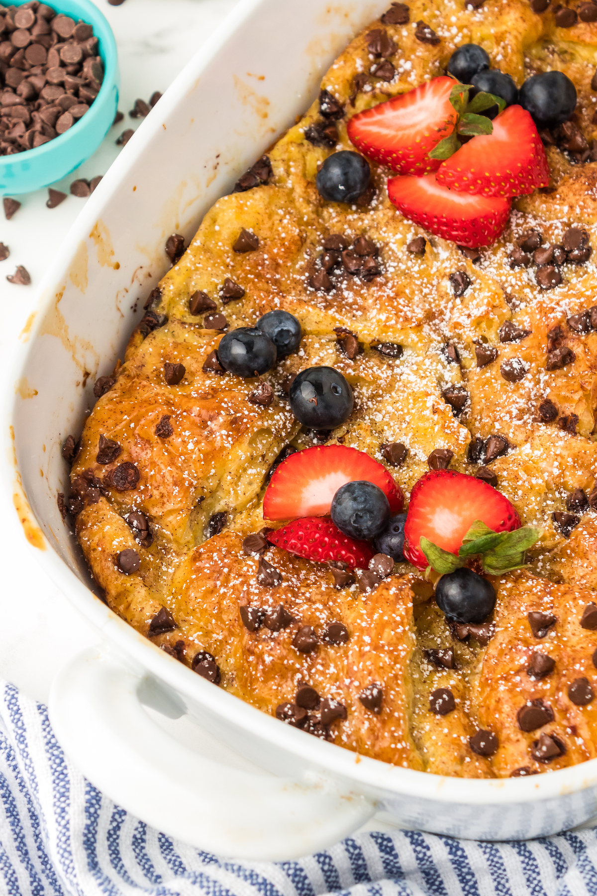 Chocolate chip croissant French toast bake in a baking dish with strawberries and blueberries on top.