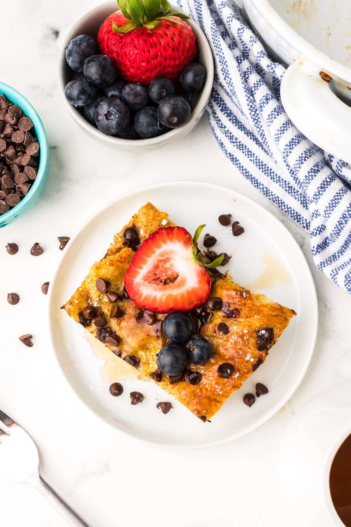 Slice of chocolate chip croissant French toast bake with chocolate chips, honey, blueberries, and strawberries.