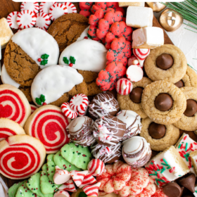 A tray filled with 7 types of christmas cookies and candies with bells and peppermint candies around the tray.