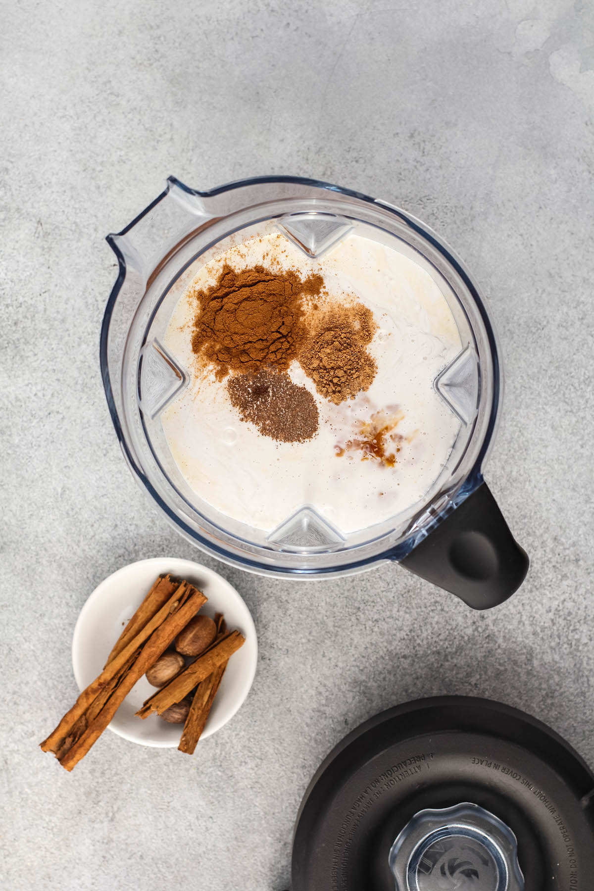 Spices and milk added to a blender with a bowl of spices next to it.
