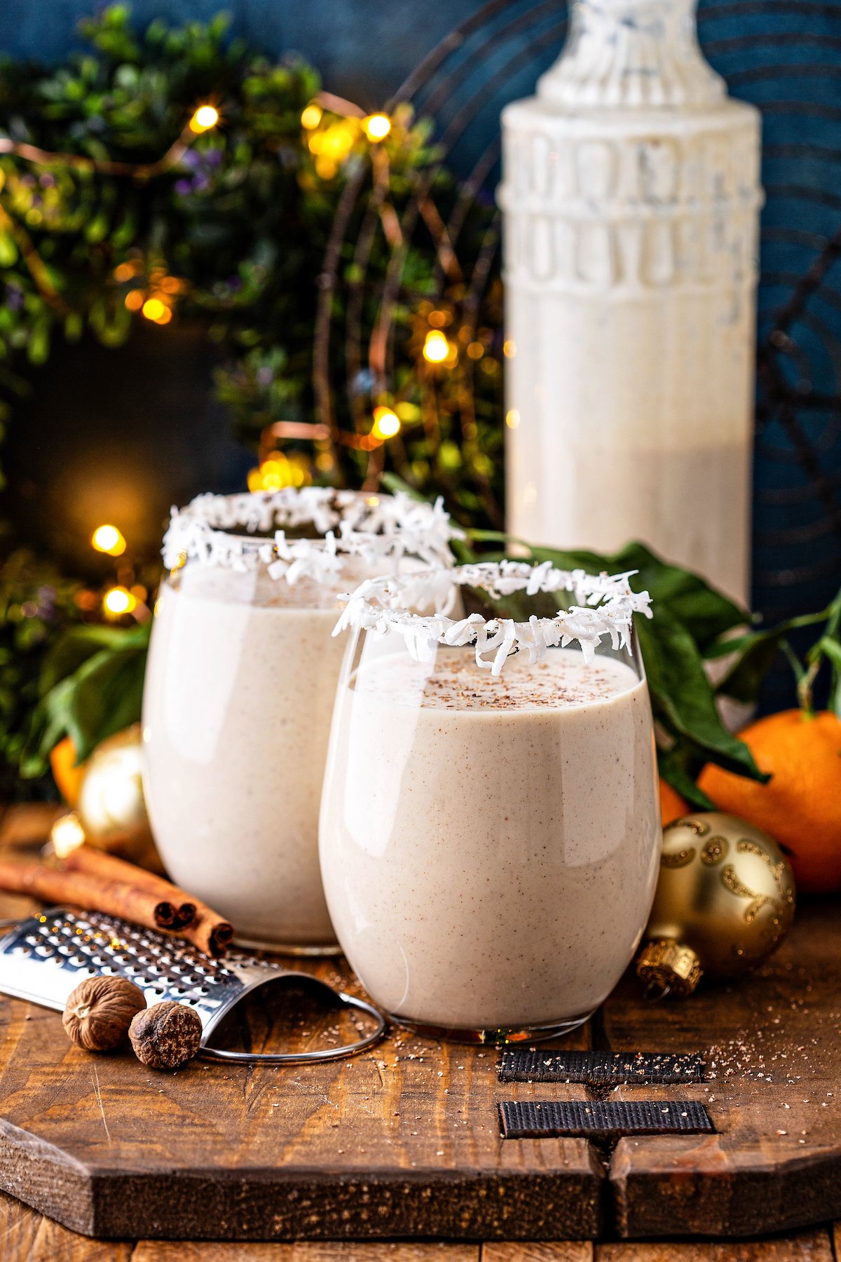 Coconut eggnog in two glasses with coconut rim and a bottle of eggnog in the background.