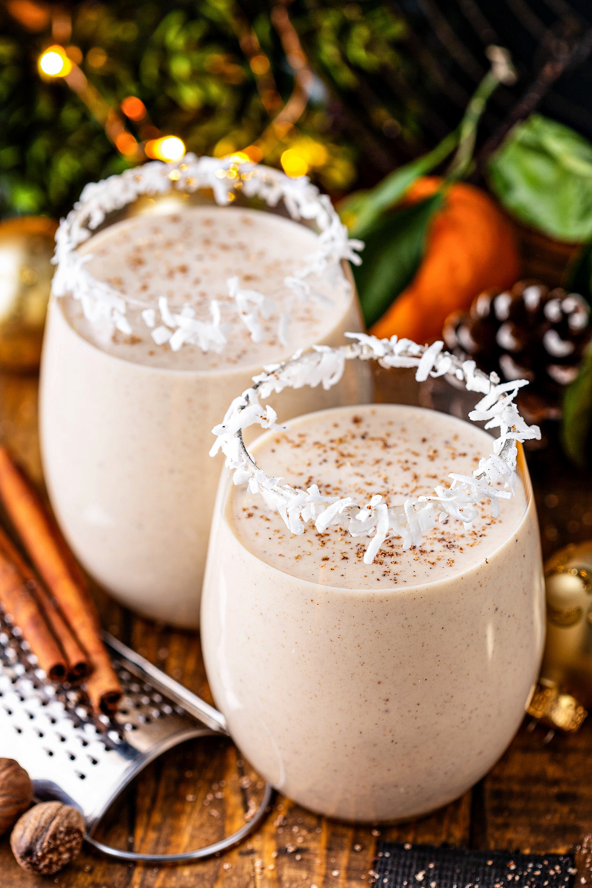 Two glasses of coquito with grated nutmeg on top and a shredded coconut rim.