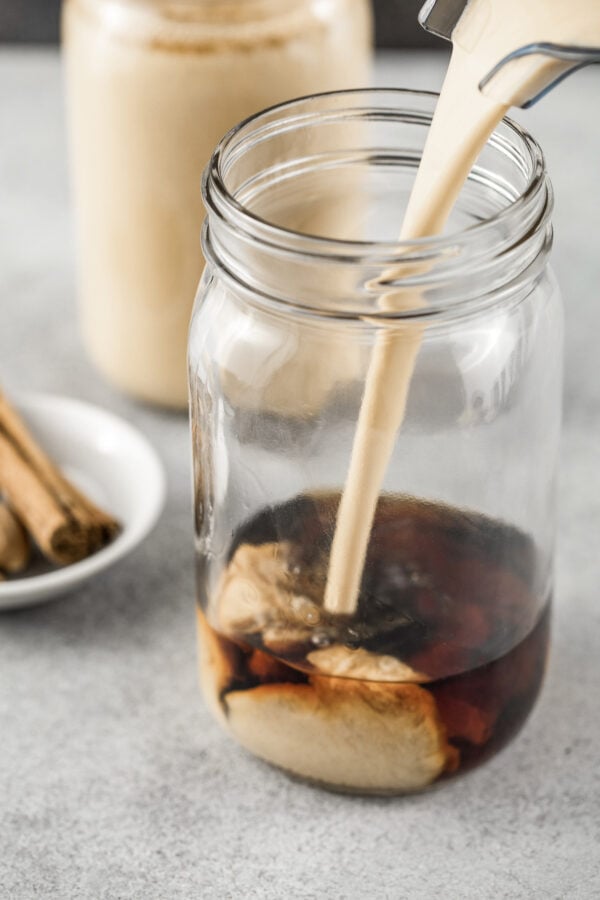 Blended coconut milk mixture being poured into a glass jar filled with rum.
