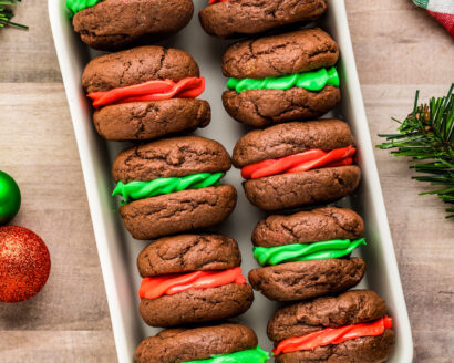 Overhead shot of chocolate whoopie pies lined up in a shallow dish, on a table with Christmas decorations.