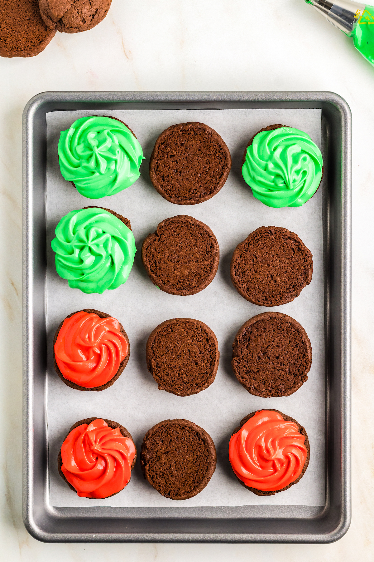 Cookie halves on a baking sheet, some frosted with green, some with red, and some not frosted.
