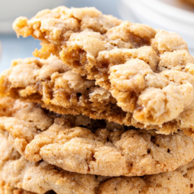 A stack of peanut butter oatmeal cookies with one cookie broken in half to show the inside.