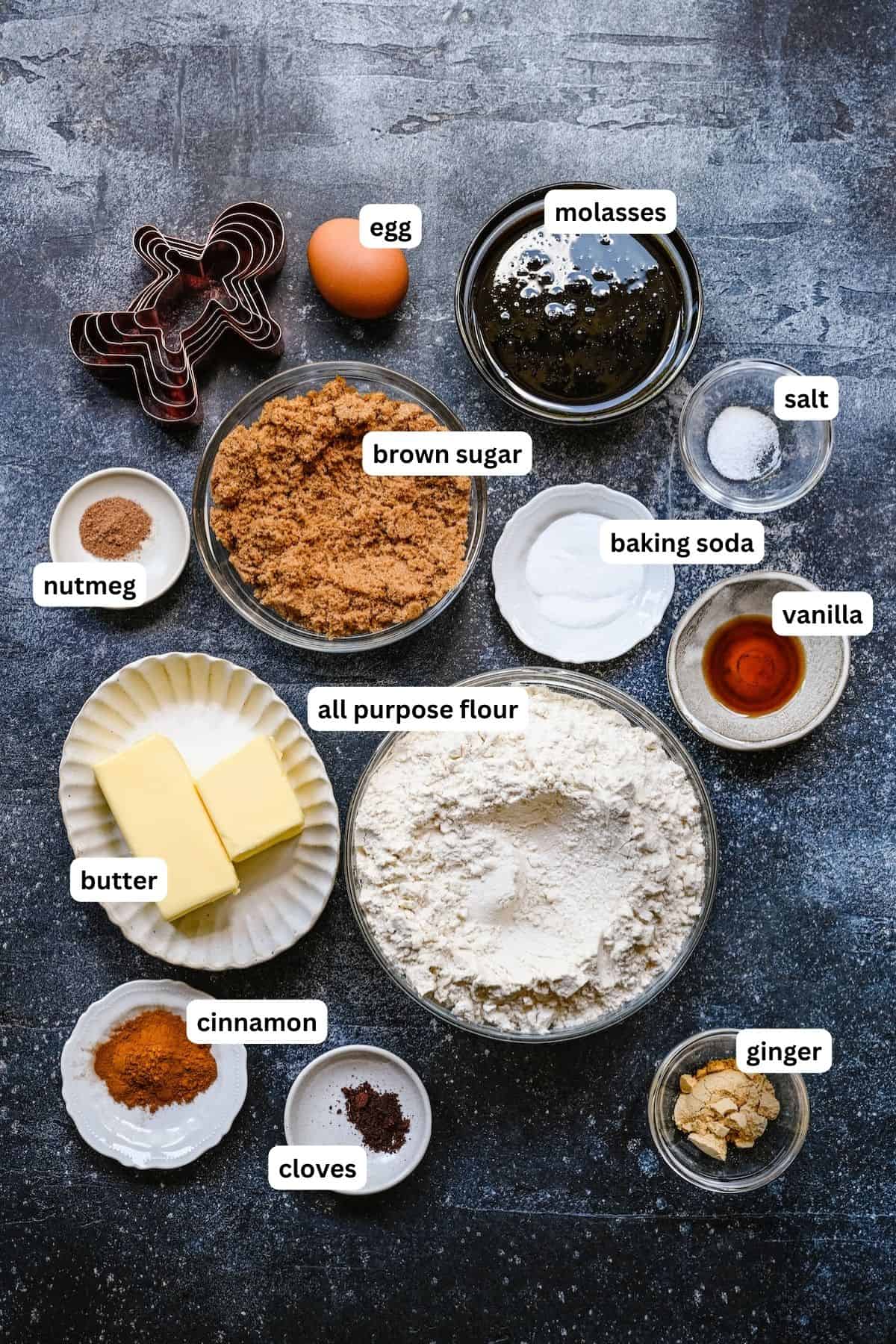 Ingredients for gingerbread man cookies recipe in order from top to bottom: egg, molasses, nutmeg, brown sugar, baking soda, salt, vanilla, butter, all purpose flour, cinnamon, cloves, ginger.