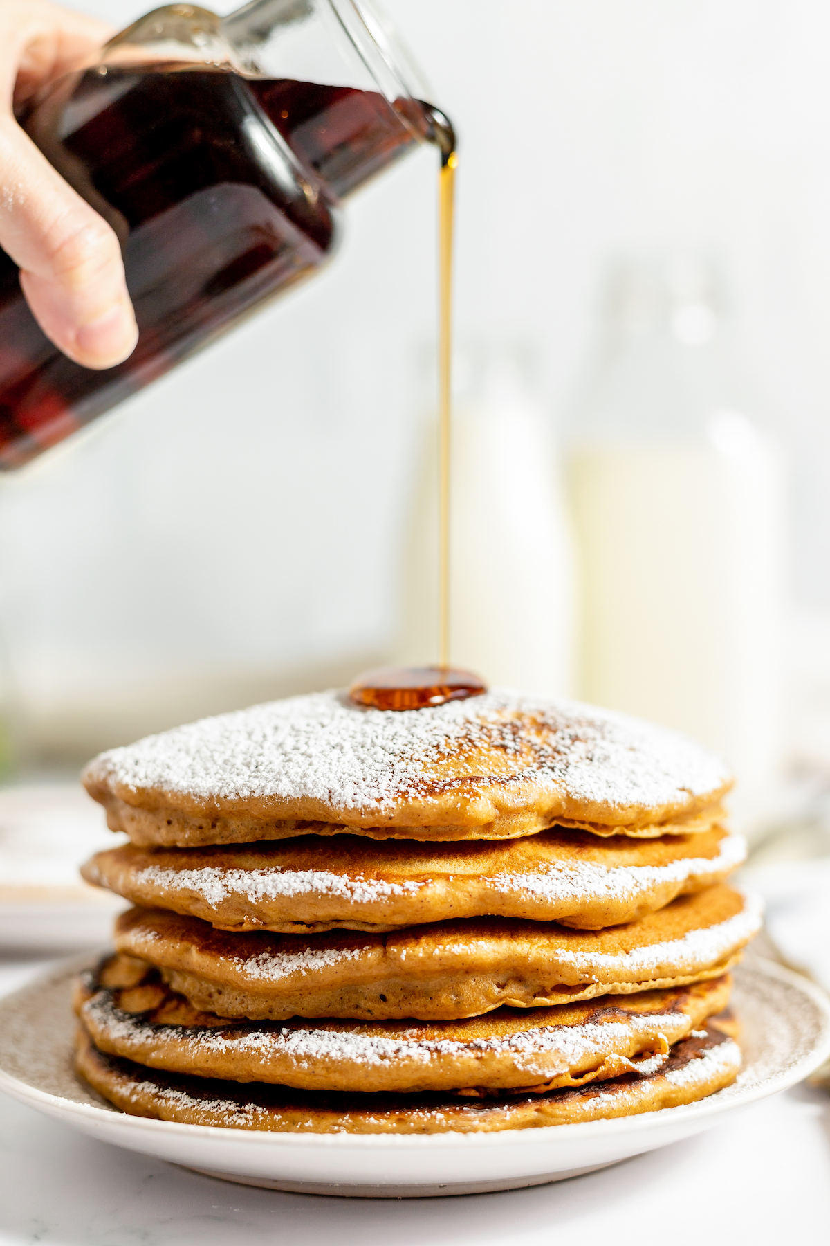 A stack of pancakes with syrup being poured over them.