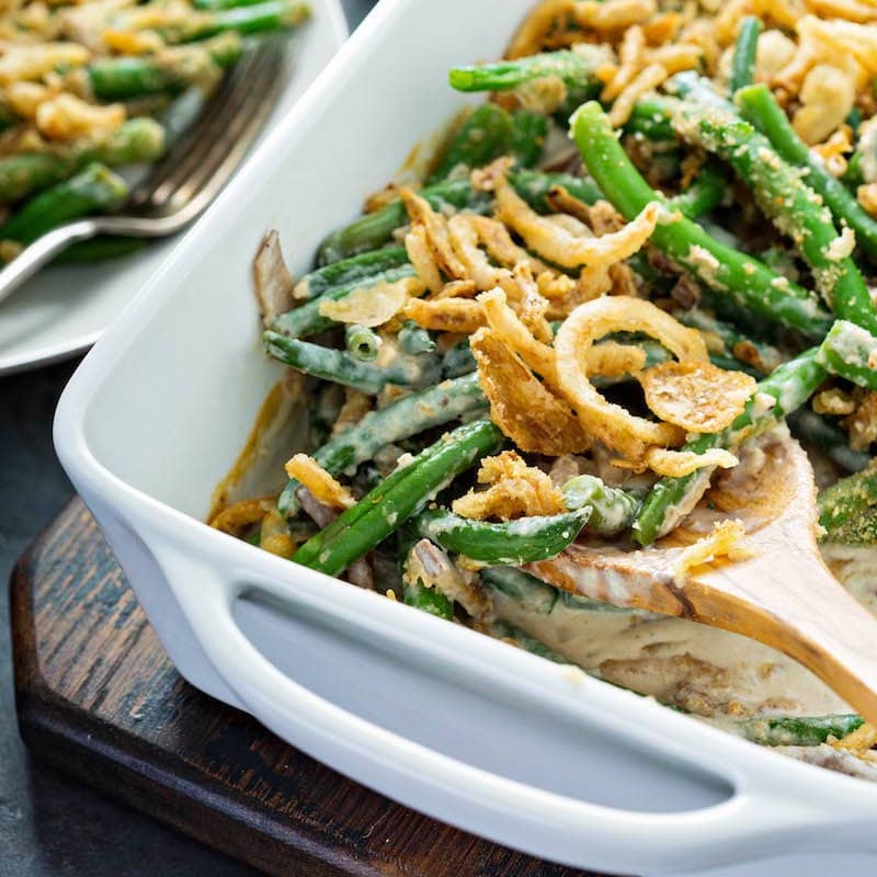 Homemade from scratch green bean casserole being scooped out of a white casserole dish with a wooden spoon.