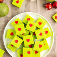 A plate of white chocolate fudge tinted green and decorated with red heart sprinkles.