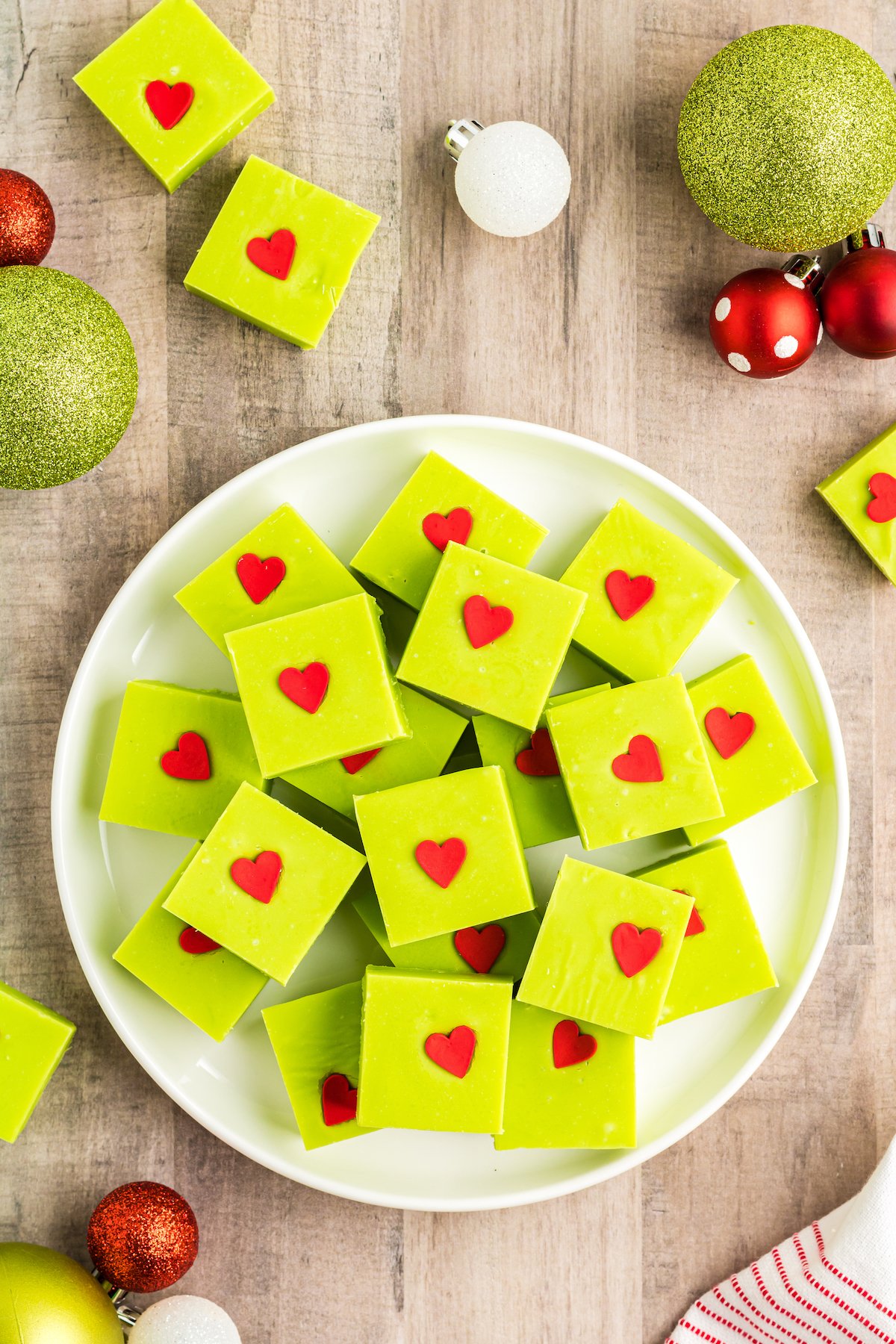 A plate of white chocolate fudge tinted green and decorated with red heart sprinkles.