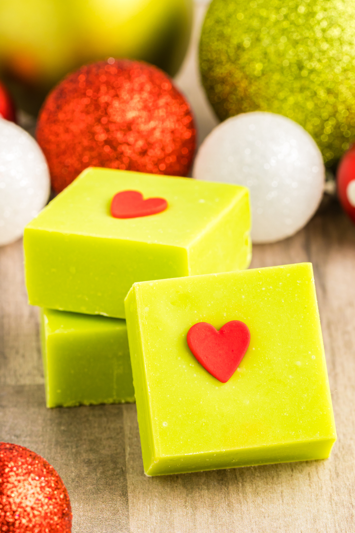 Grinch fudge squares with a backdrop of red and green ornaments.