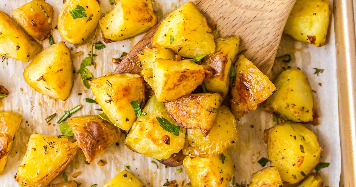 Crispy potatoes on a baking sheet with a wooden spoon.