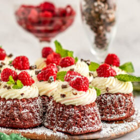 Red velvet bundt cakes with cream cheese frosting, powdered sugar, and a raspberry on top.