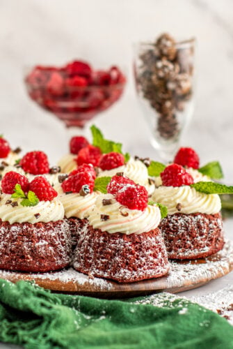 Red velvet bundt cakes with cream cheese frosting, powdered sugar, and a raspberry on top.