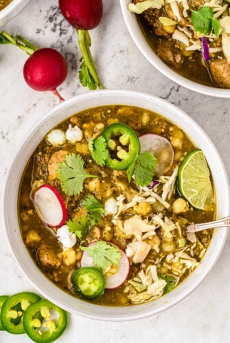 Pork pozole verde with cilantro, jalapeño, radishes, and a lime wedge.