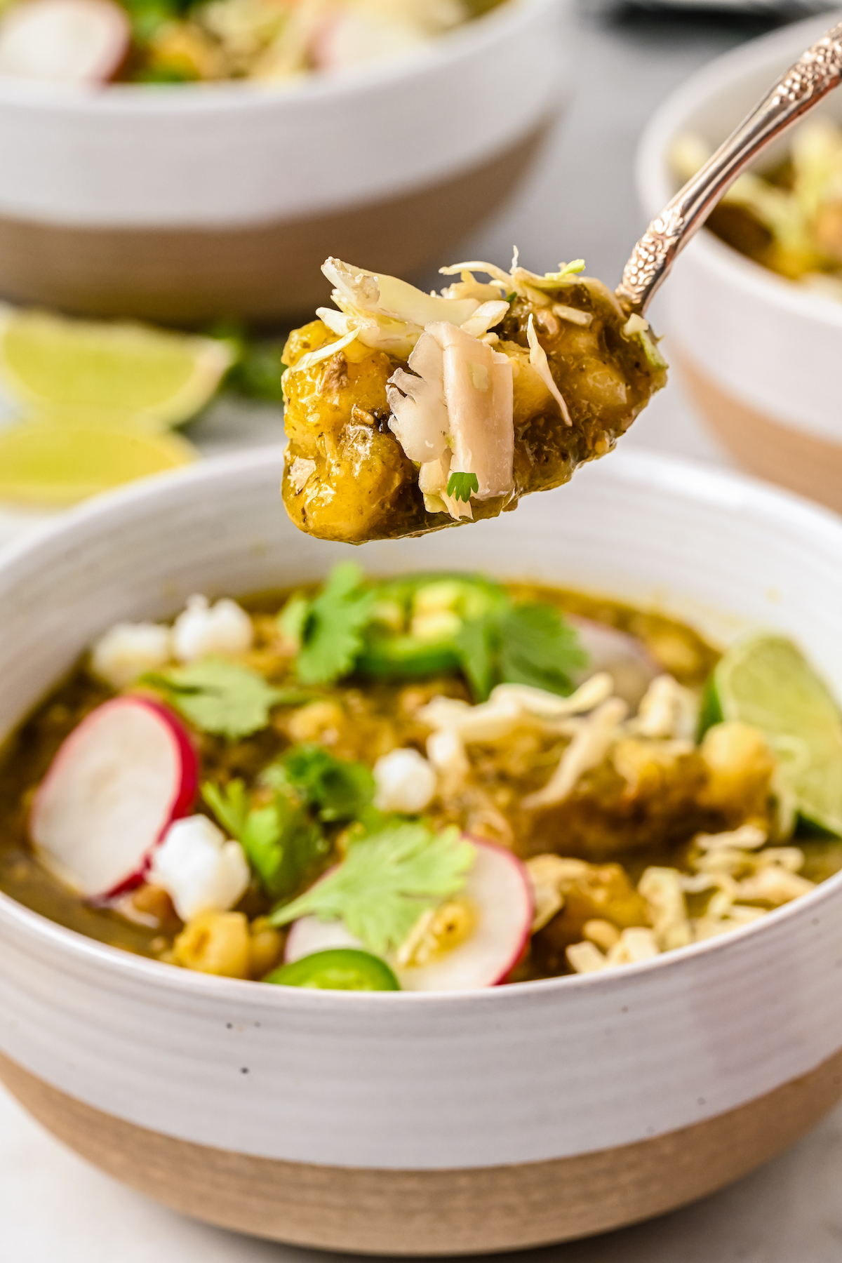 Spoonful of pork pozole verde over a serving bowl.