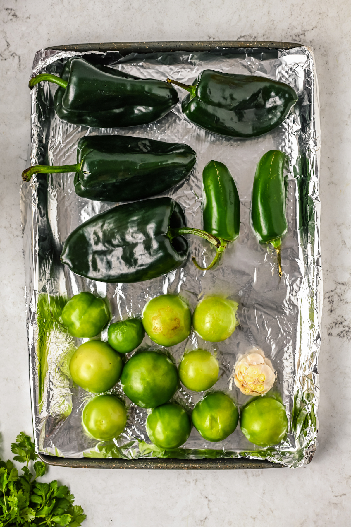 Poblanos, tomatillos, and jalapeños in a foil-lined tray.