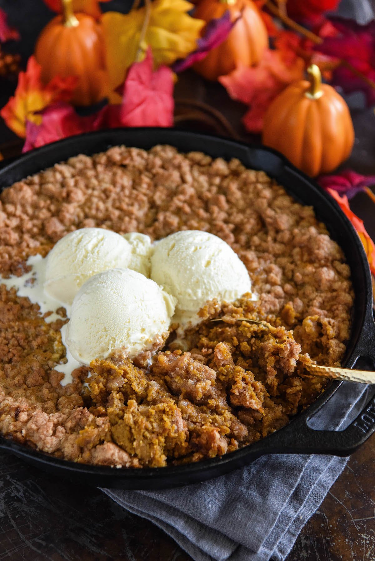 A spoon scooping up pumpkin crisp from a cast iron skillet.
