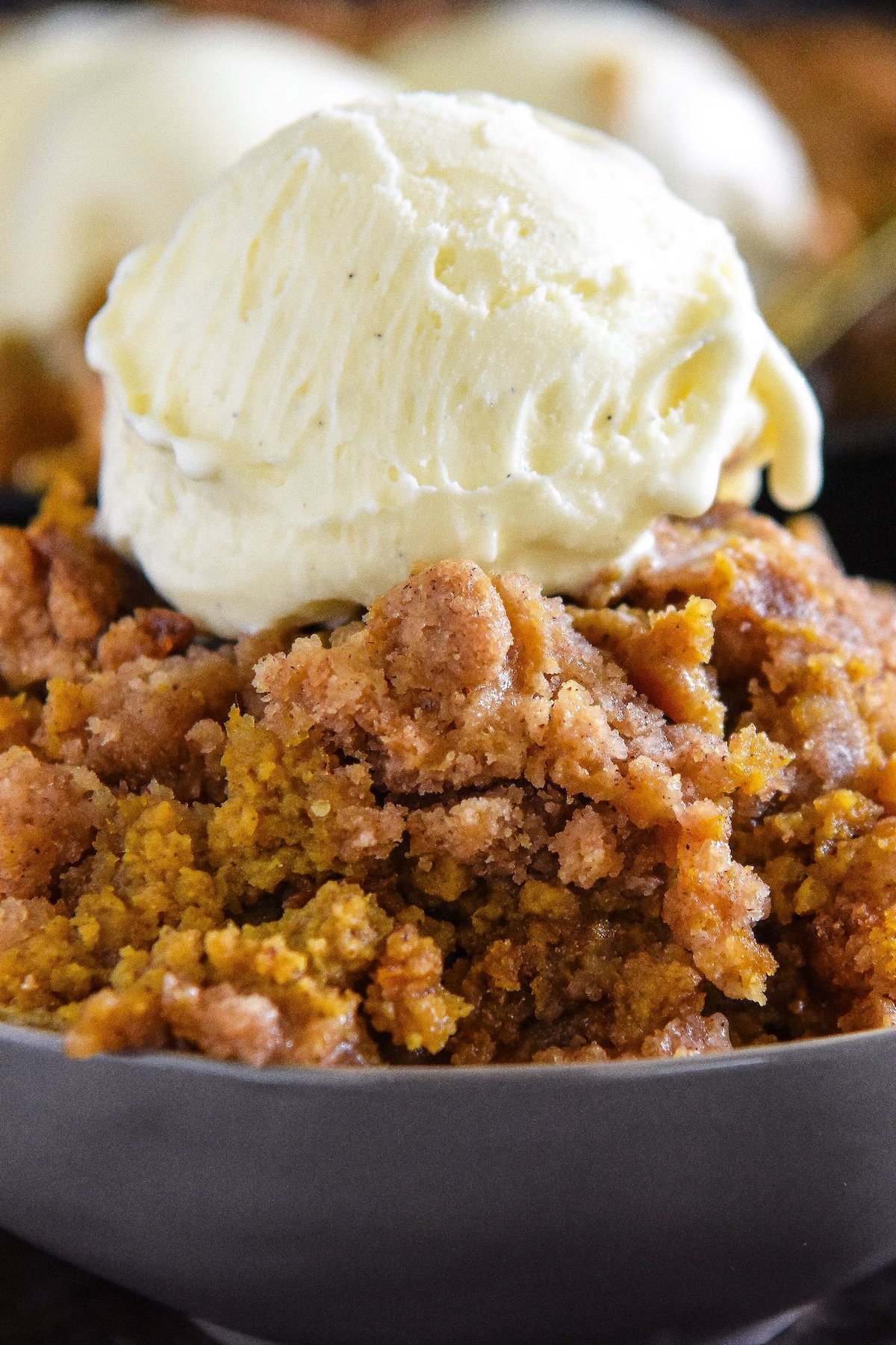 Pumpkin crisp in a bowl with vanilla ice cream on top.