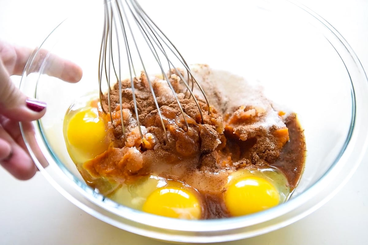 A whisk stirring eggs, pumpkin puree, cinnamon, sugar and more.