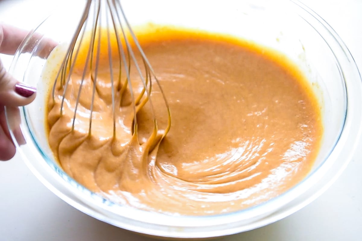 A whisk stirring pumpkin pie filling in a bowl.