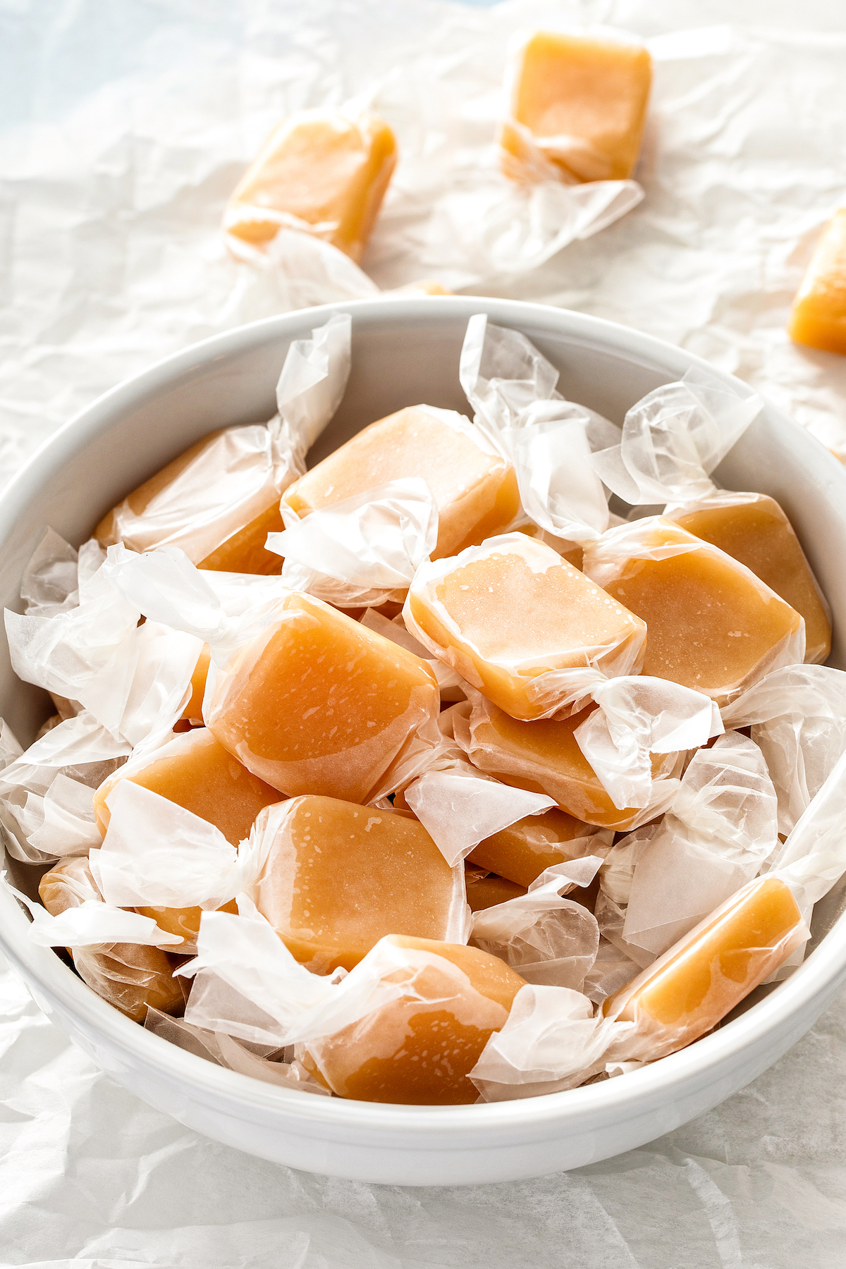 Soft rum caramels wrapped with parchment paper in a bowl.