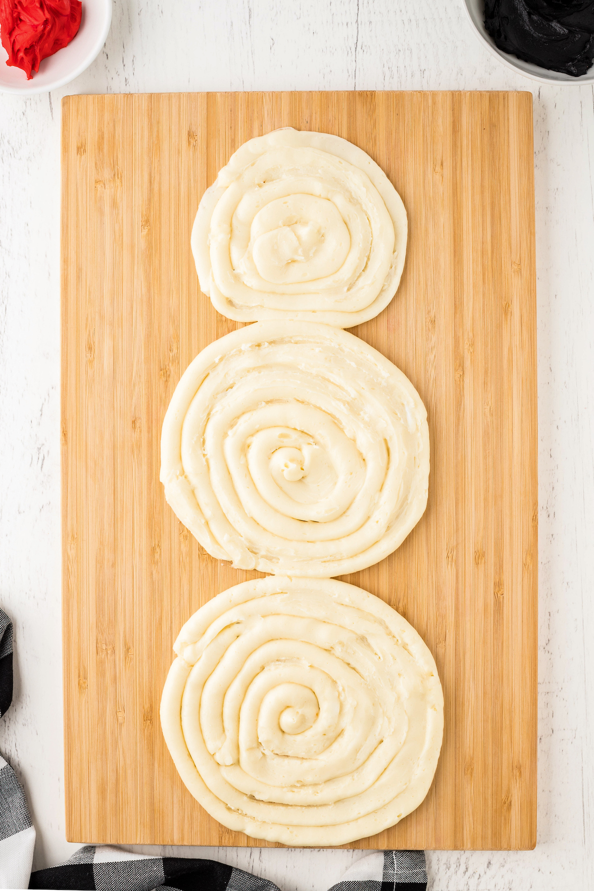 Three circles of white frosting on a wooden board.