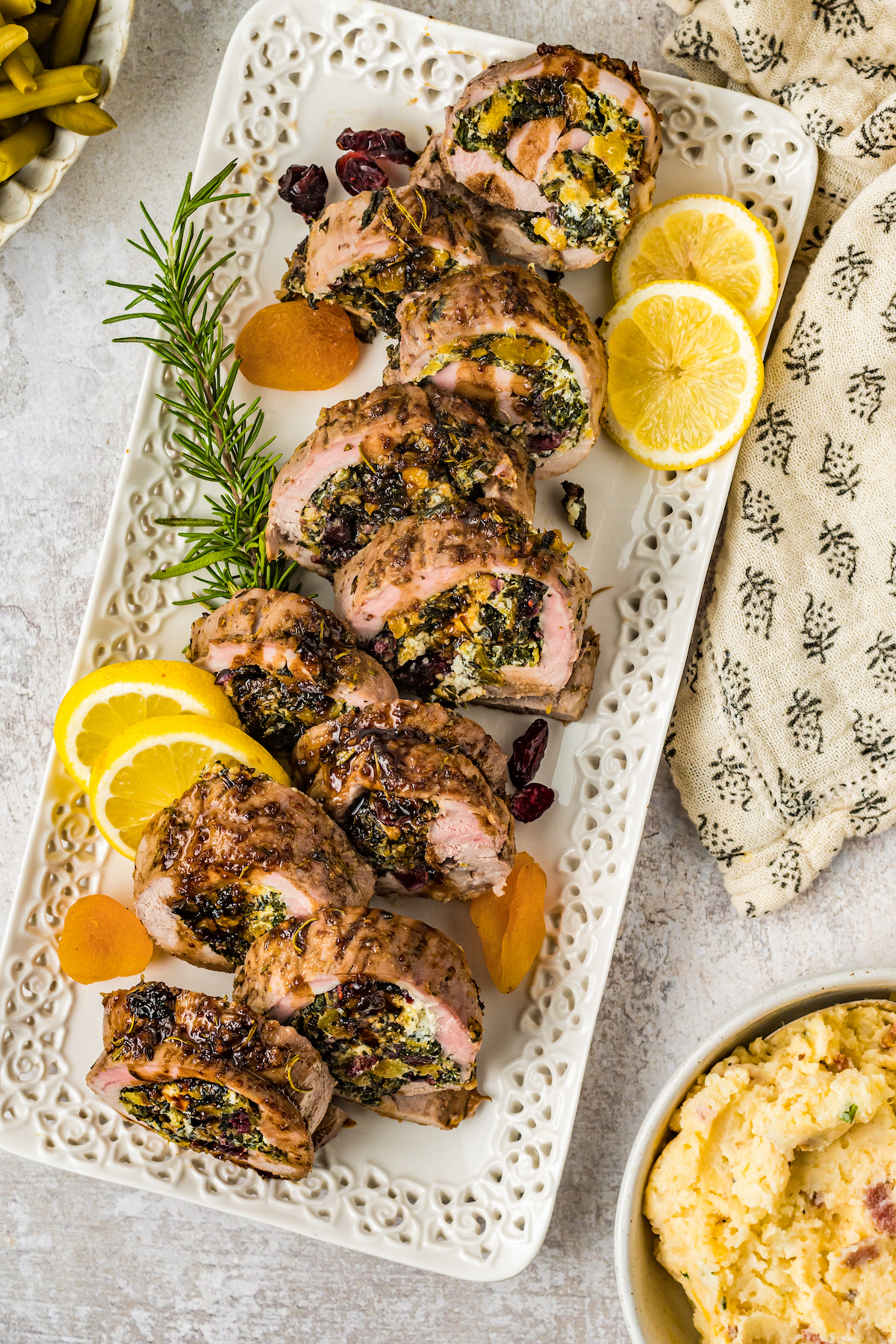 Sliced stuffed pork loin in a large plate with lemon wedges. 