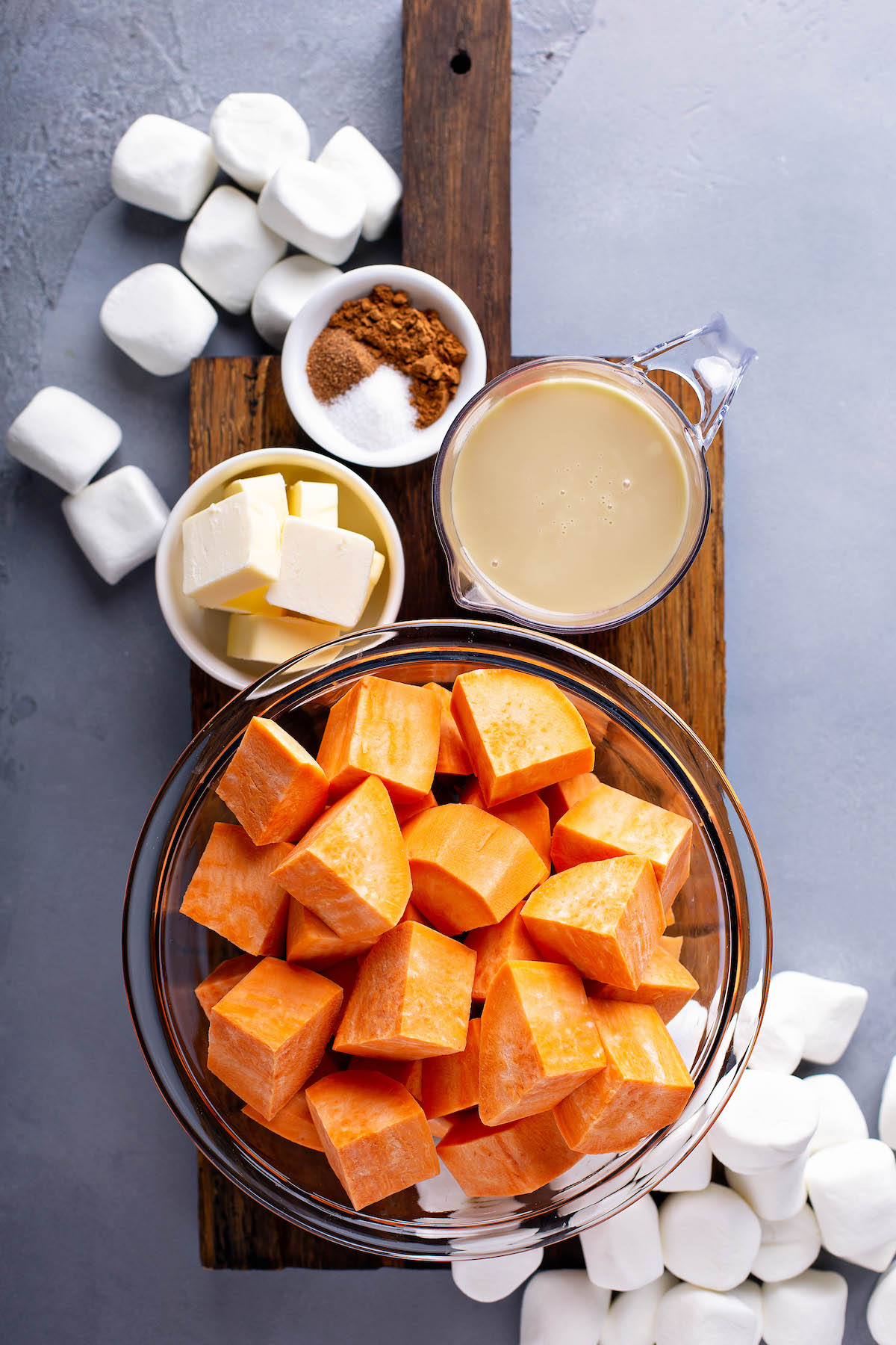 Bowls of ingredients for sweet potato casserole recipe arranged on top of a chopping board.