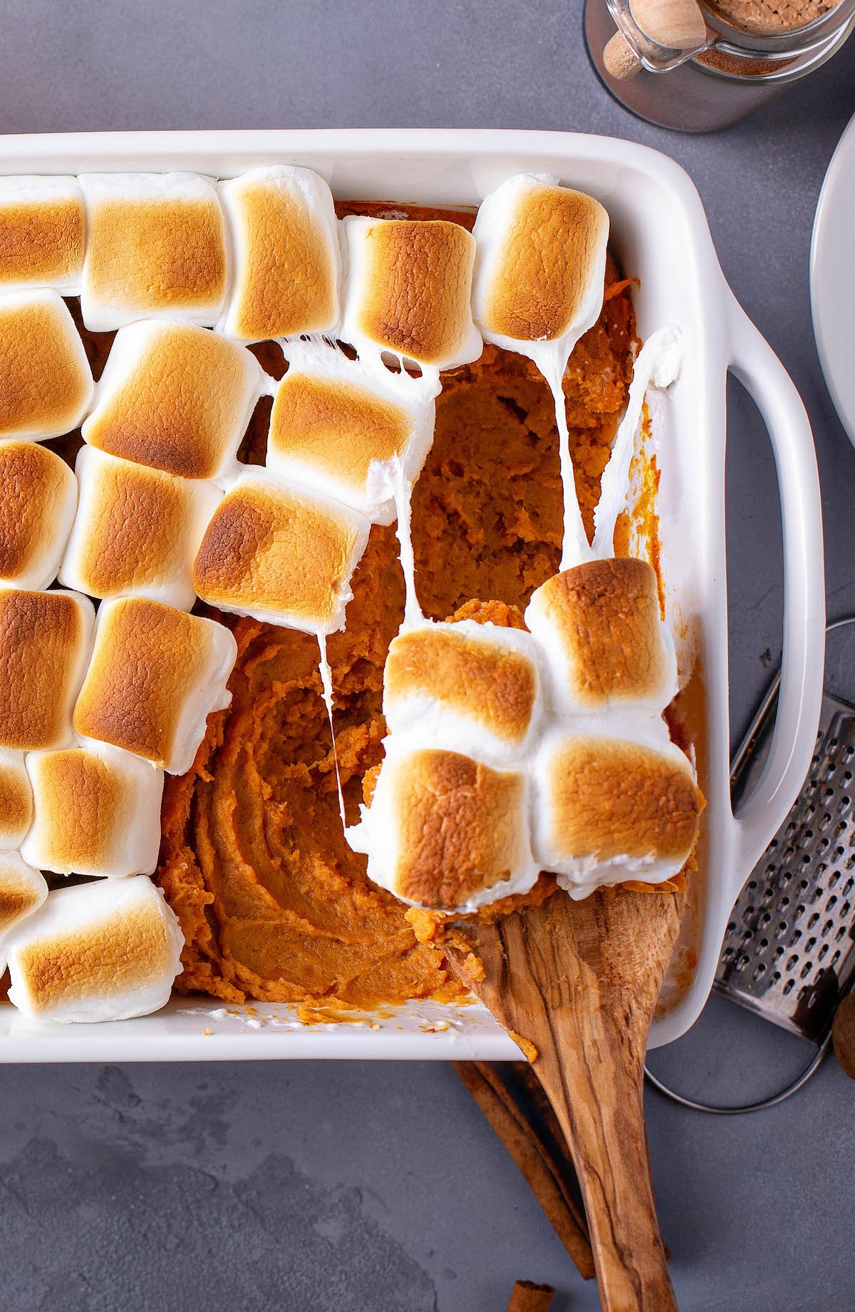 A wooden spoon scooping a serving of sweet potatoes out of a casserole dish.