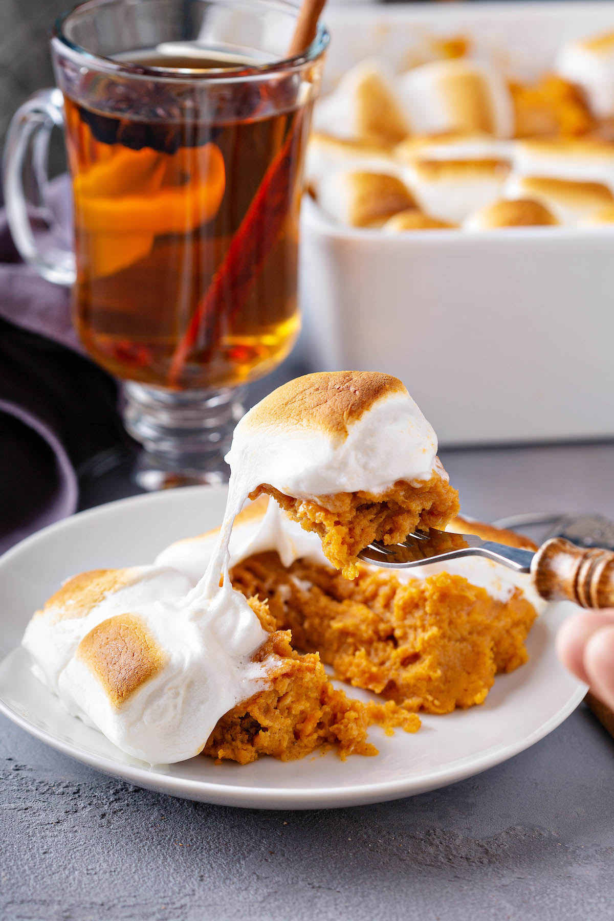 A fork picking up a bite of sweet potatoes with melted toasted marshmallows on top.