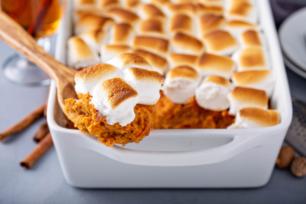 A wooden spoon scooping out a serving of sweet potato marshmallow casserole.