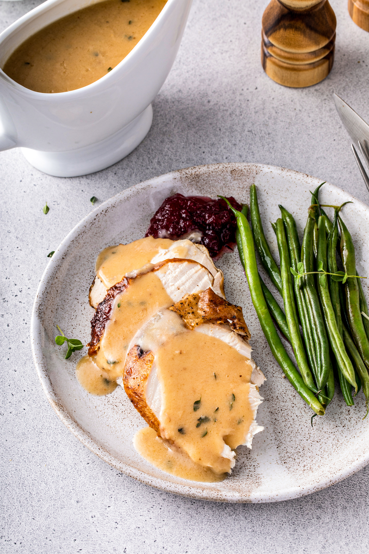 Gravy drizzled over turkey on a plate with green beans. 