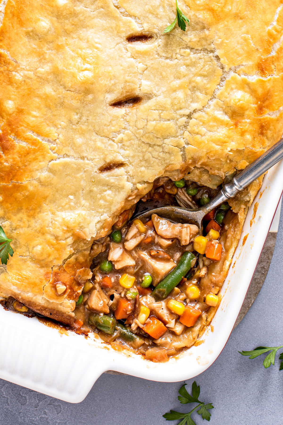 Turkey pot pie in a casserole dish with a spoon scooping up a serving.