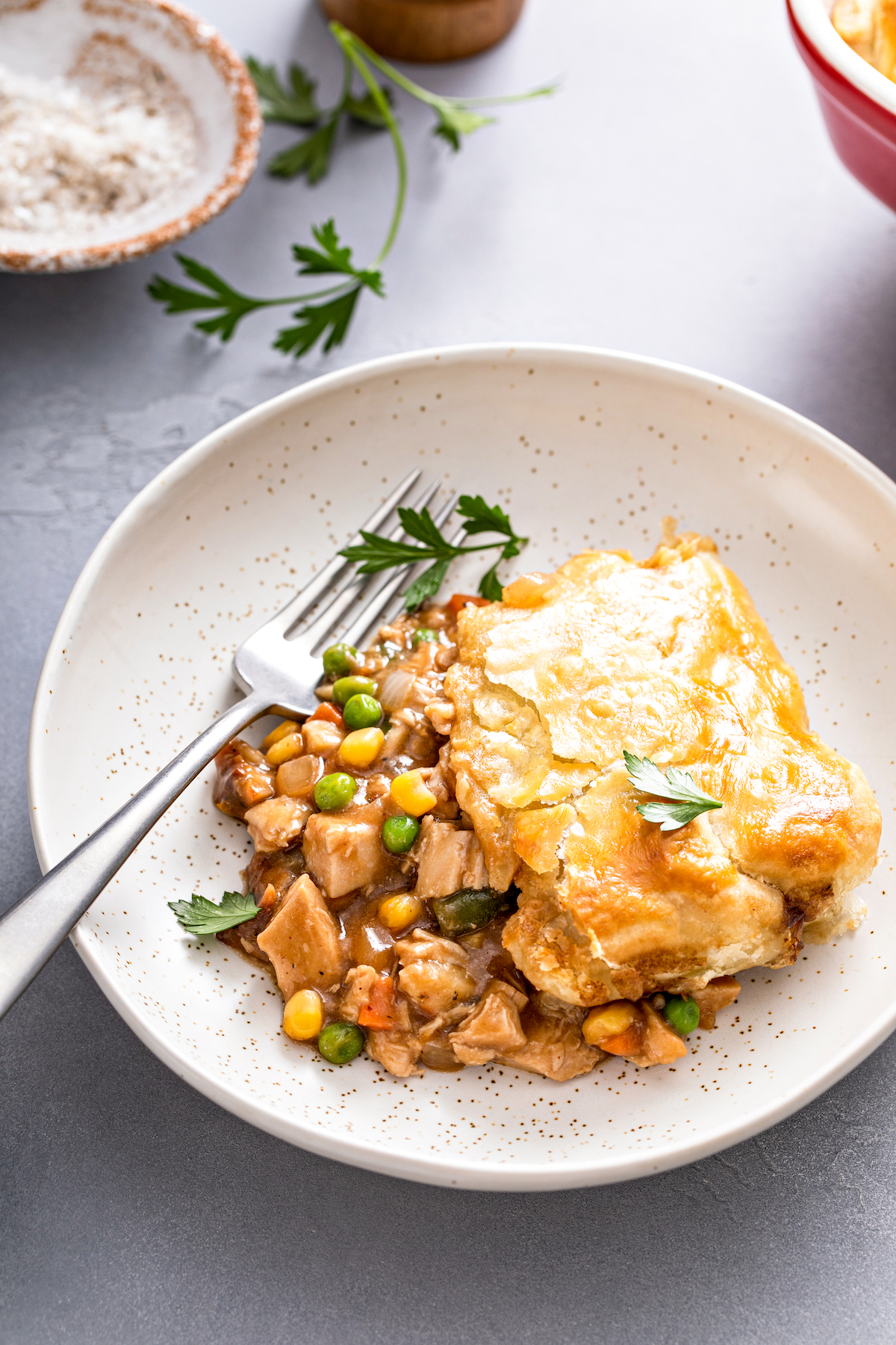 A fork on a plate with puff pastry pot pie with fresh herbs on top.