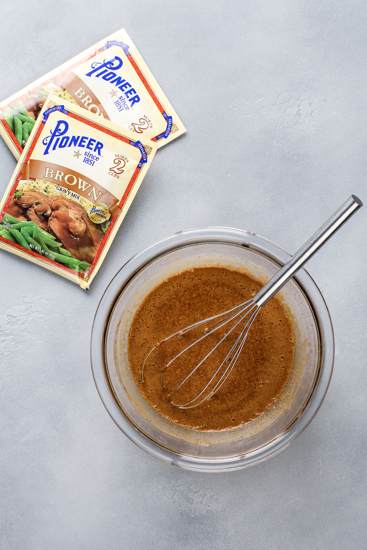 A bowl with beer and brown gravy whisked together and two packets of Pioneer brown gravy mix.