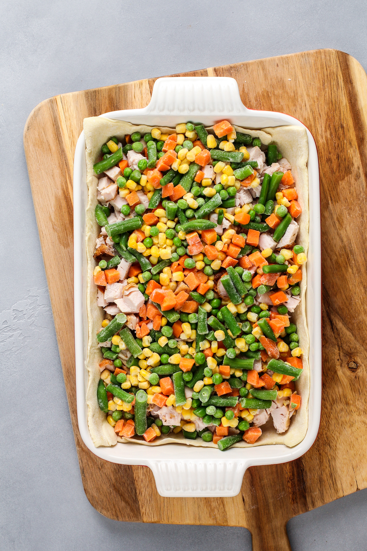 Mixed vegetables on top of turkey in a puff pastry lined casserole dish.