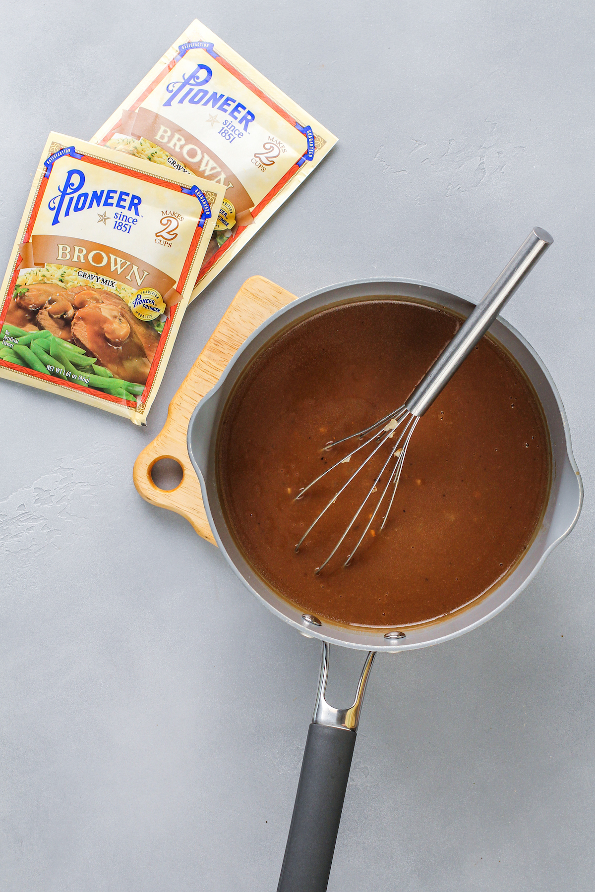 A sauce pan with brown gravy and a whisk in it.