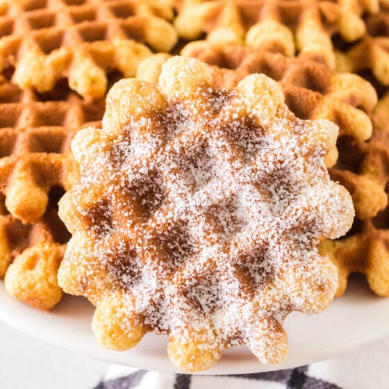 Vanilla waffle cookies on a plate. One of them has powdered sugar.