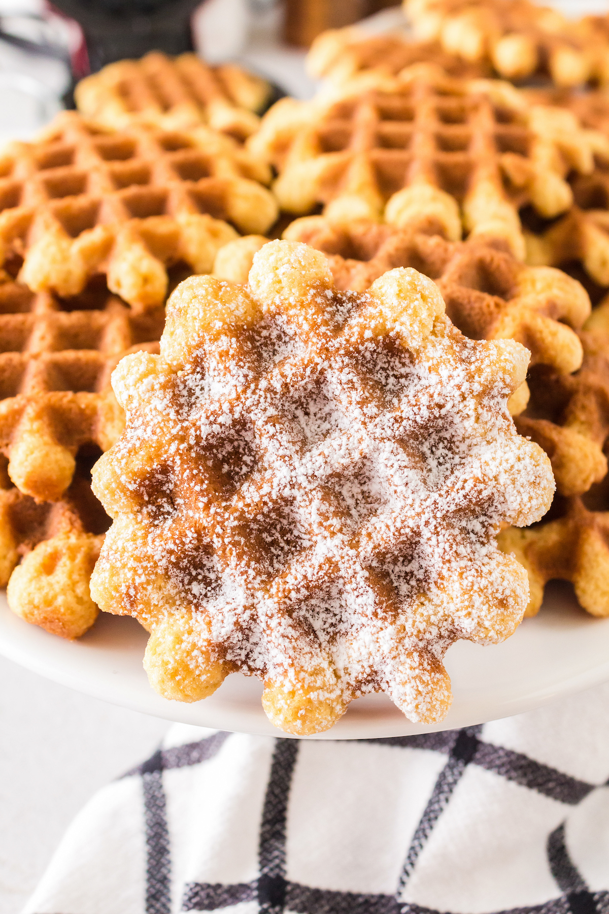 Vanilla waffle cookies on a plate. One of them has powdered sugar.
