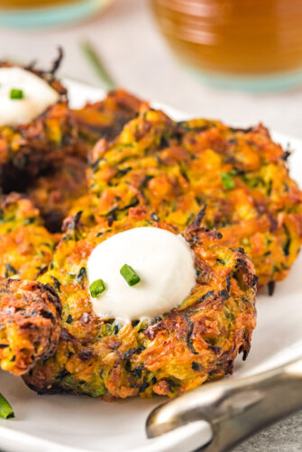 Air-fried zucchini fritters with sour cream and chives on a white serving dish.