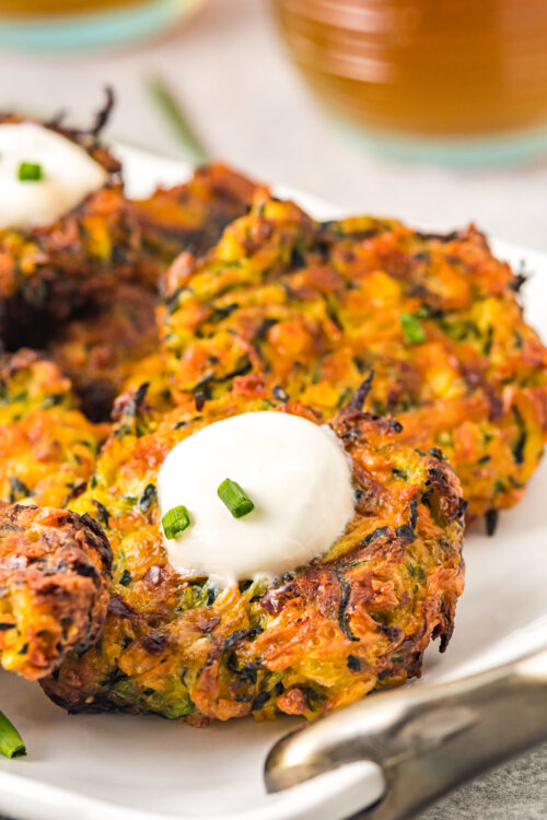 Air-fried zucchini fritters with sour cream and chives on a white serving dish.