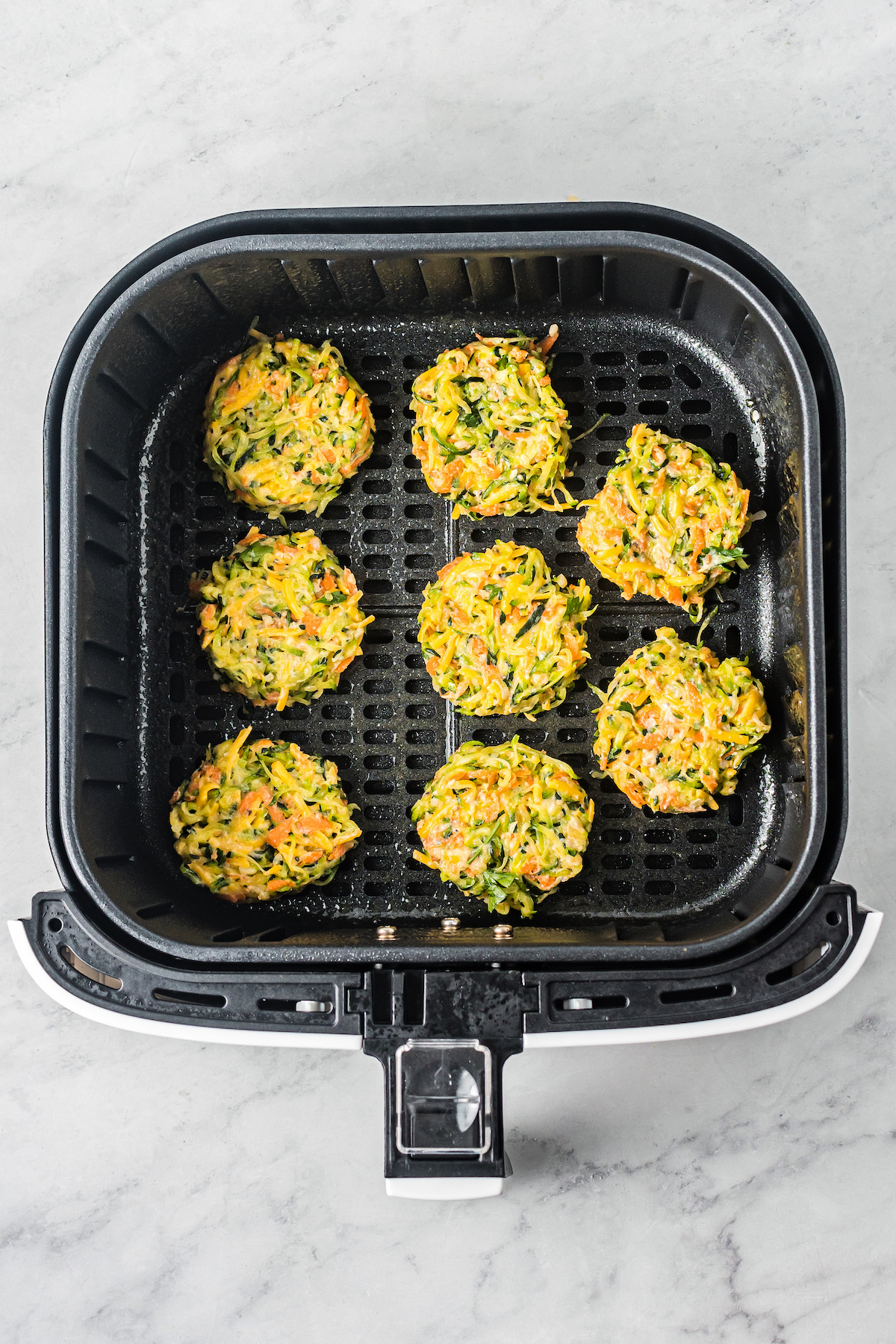 Veggie fritters lined up in the basket of an air fryer.