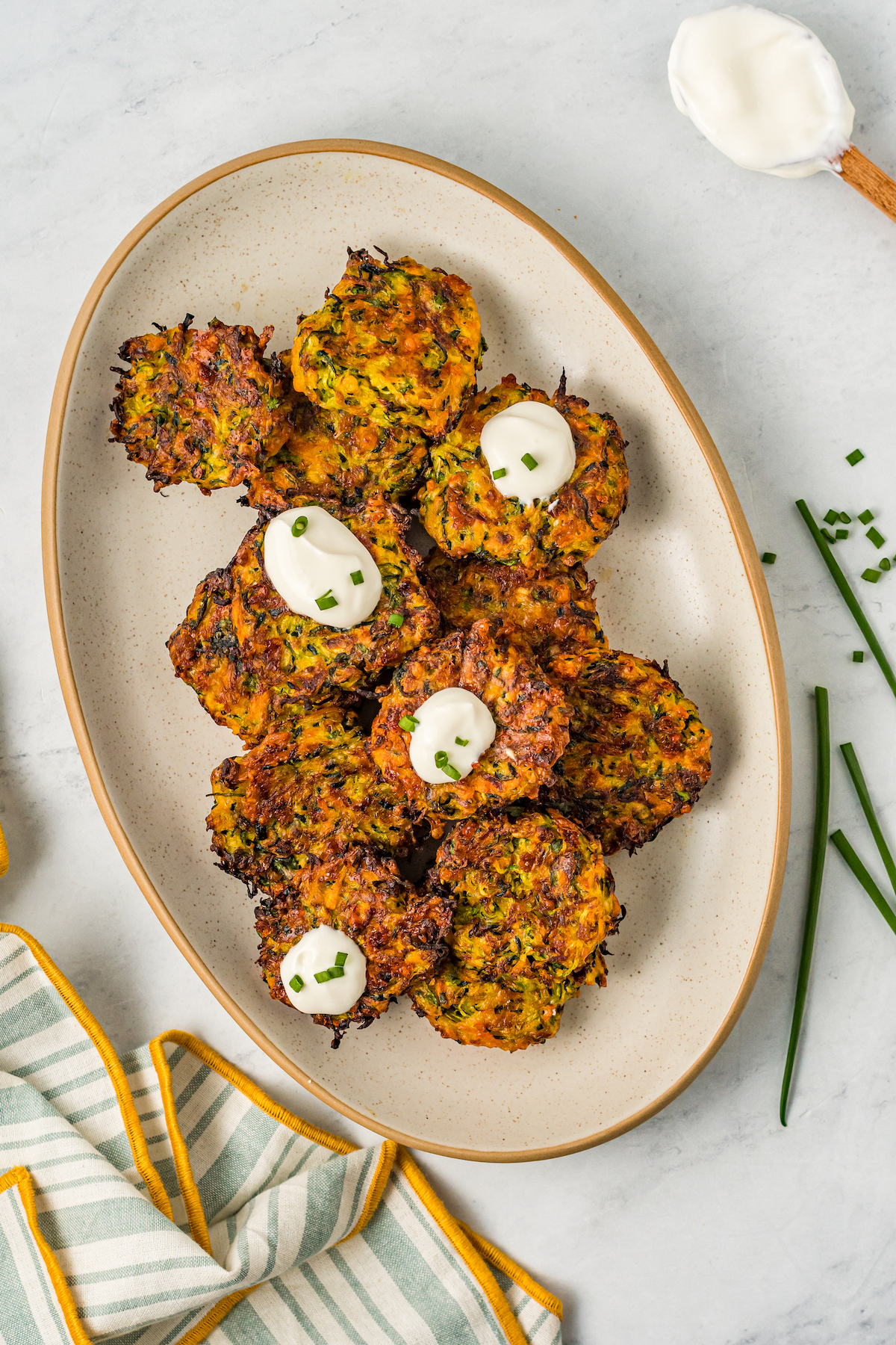 A platter of homemade zucchini fritters, garnished with dollops of sour cream and fresh herbs.