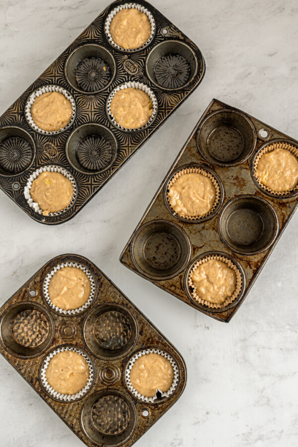 Muffin tins with muffin liners in every other well. The muffin liners are partially filled with batter.