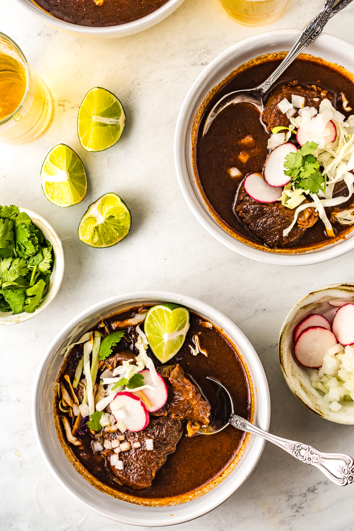 Two bowls of beef birria with toppings.