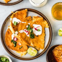 Tacos de birria in a plate topped with crema, cilantro, and onion.