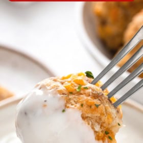 A sausage ball on a fork dipped in white gravy.