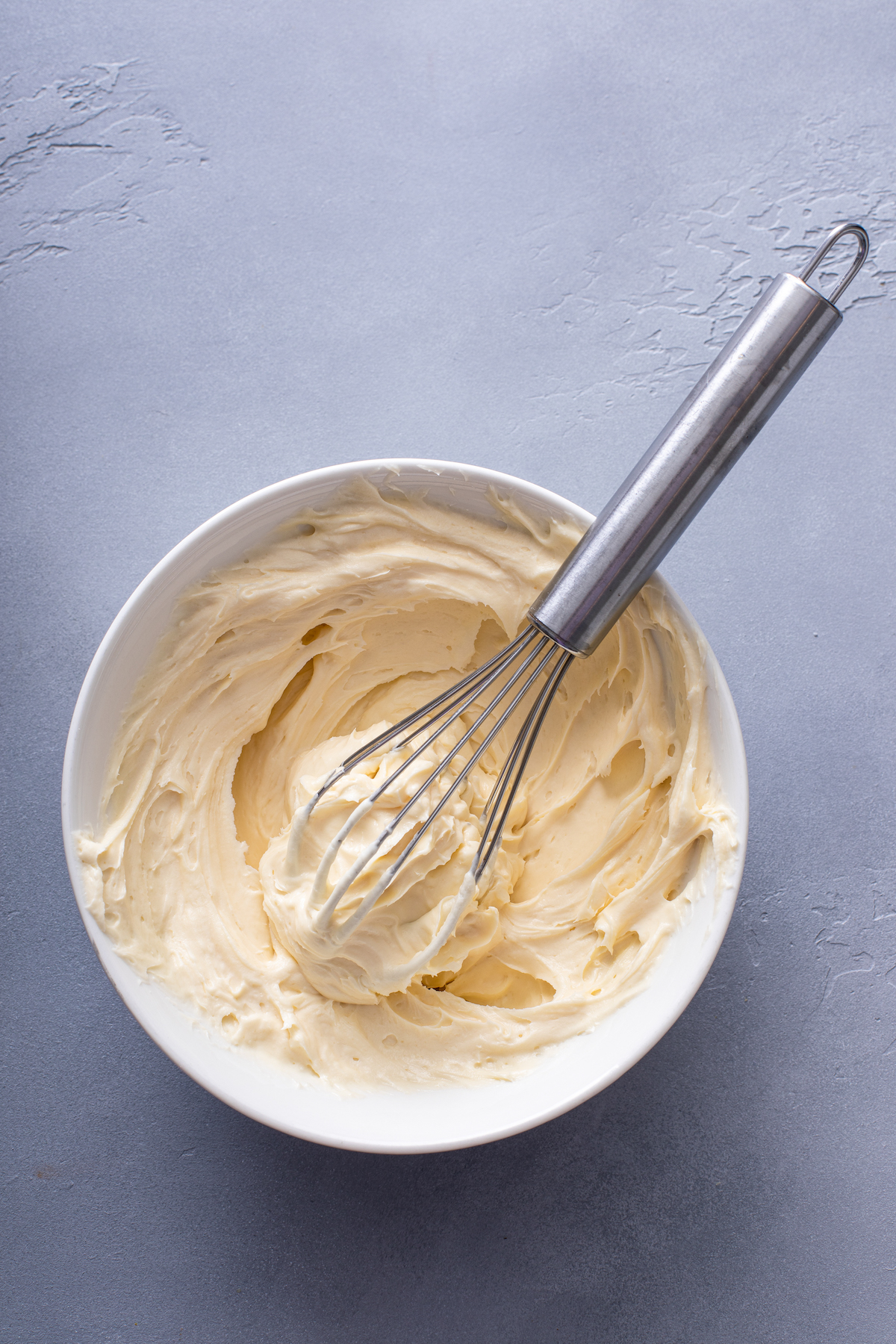 Cream cheese filling in a bowl with a whisk.